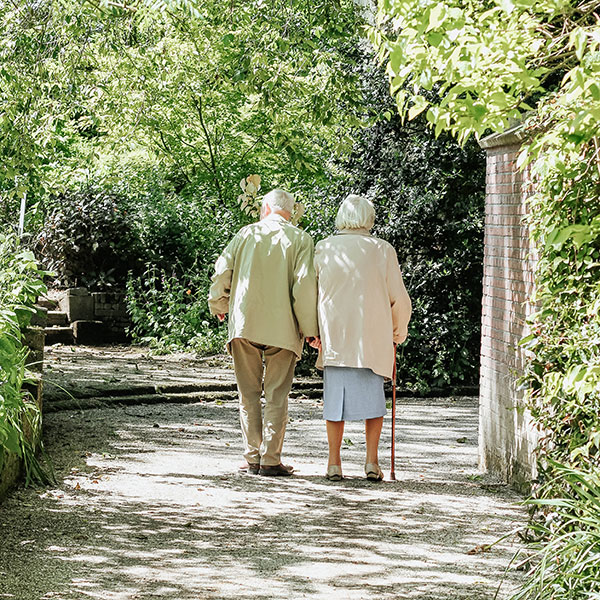 An elderly couple walking along a path of trees and shrubs