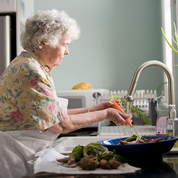 An elderly woman washing carrots in the sink