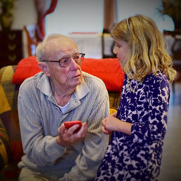 Seated old man holding phone while talking to a young girl